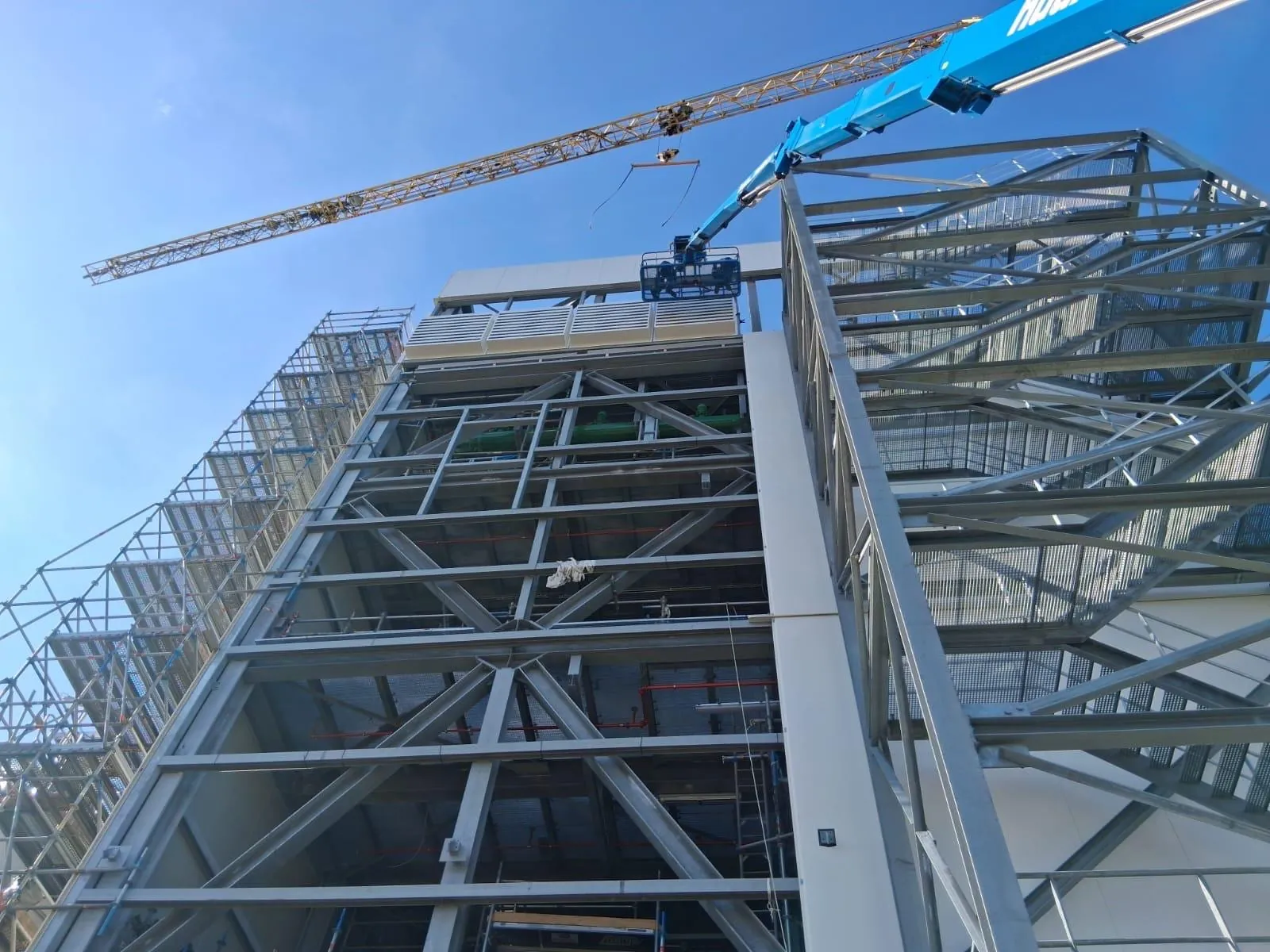 Staalconstructie met geluidswerende roosters tijdens montage op hoogte, met torenkraan en hoogwerker