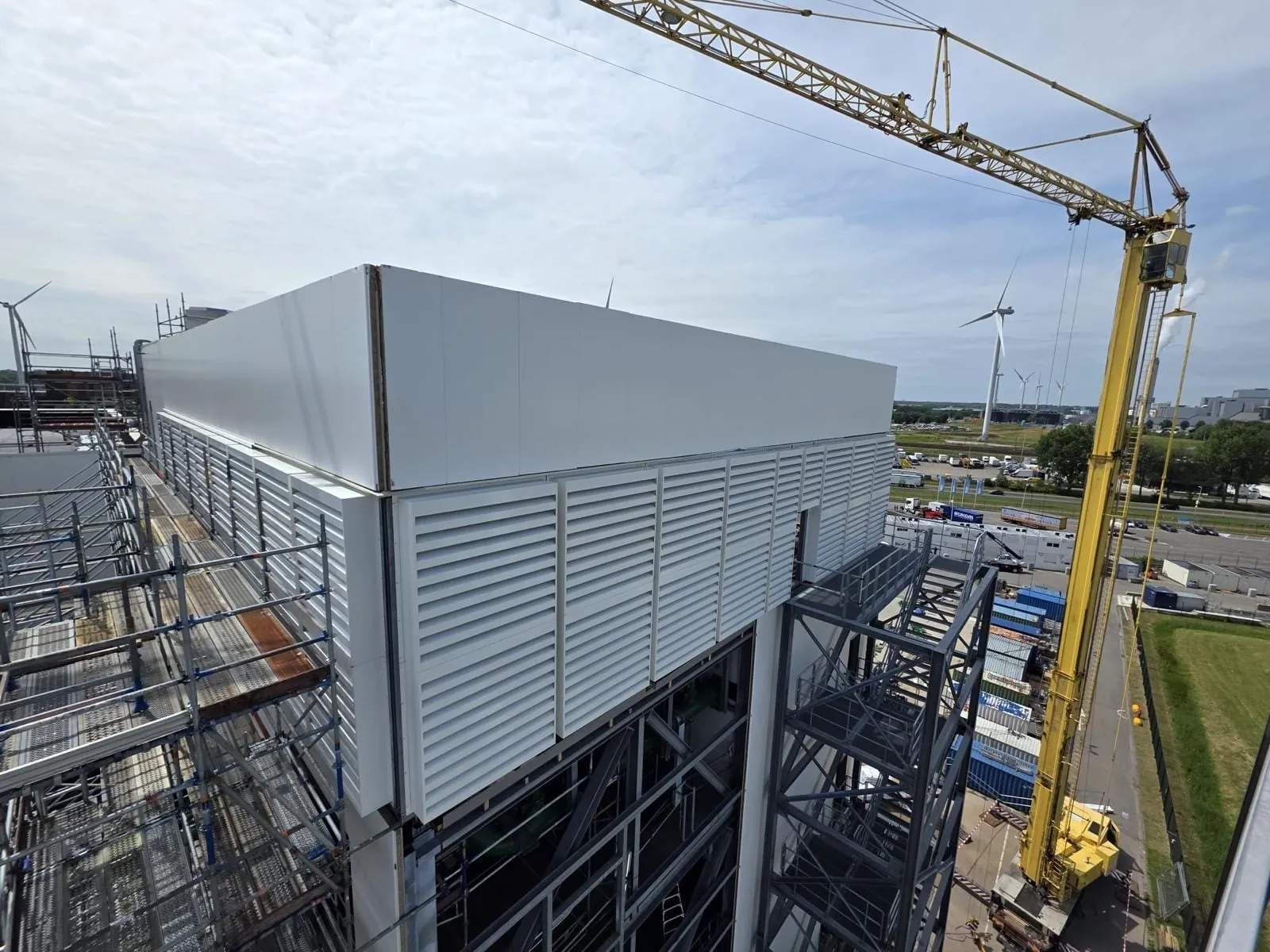 Staalconstructie en gevelbeplating van een industriële hal, gezien vanaf hoogte met torenkraan